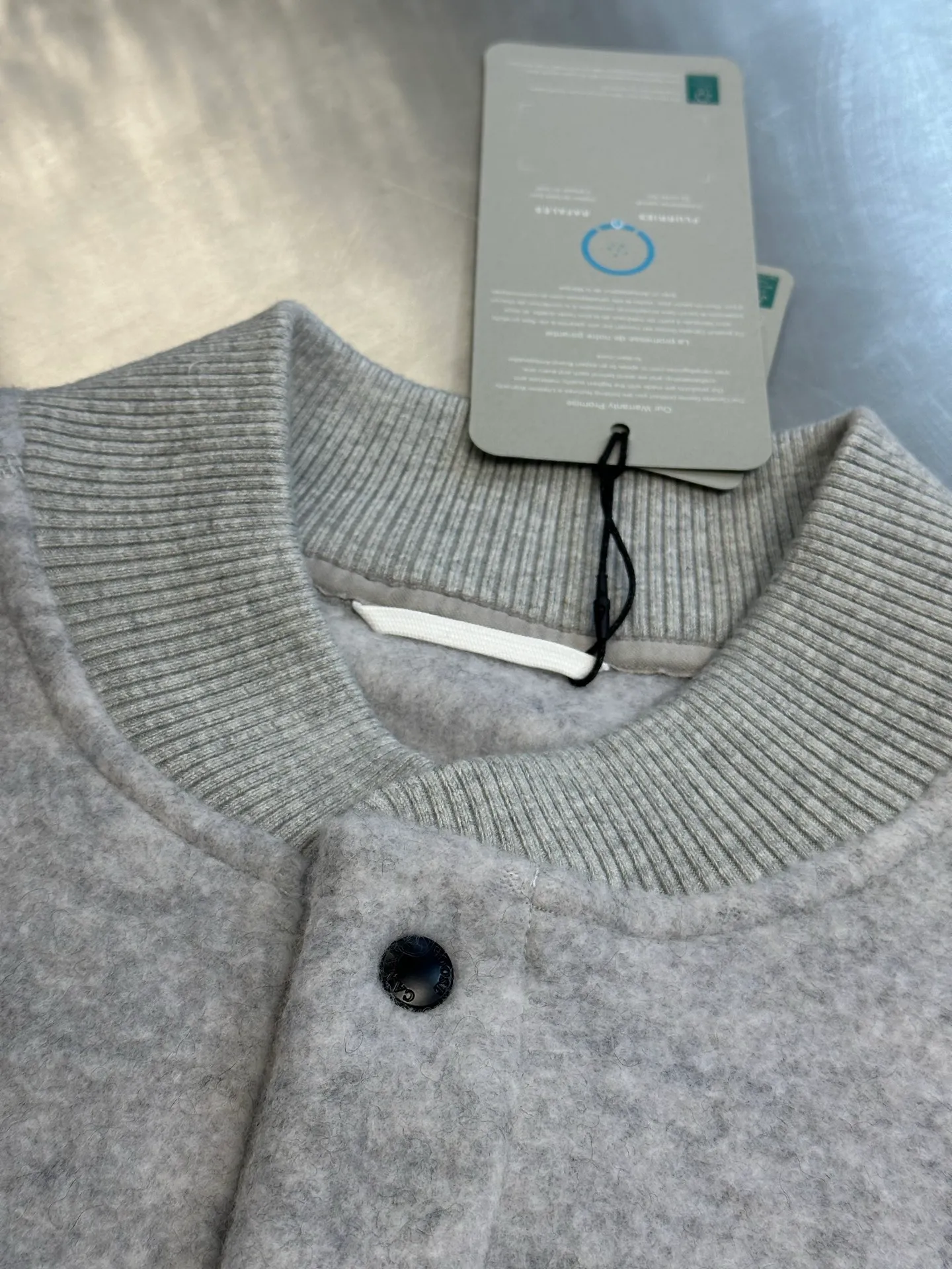 P770 Canada Goose Fleece Badge Button Jacket The main fabric of this jacket is light gray wool blend fabric to improve the fabric's wear resistance, wrinkle resistance and warmth. Wool provides good warmth and a natural feel, while blended fibers enhance the fabric's practicality and durability.  The cutting process needs to ensure that the texture and color of the fabric are evenly distributed, especially with this light gray tone, to avoid chromatic aberrations. The stretchability of wool-blend fabrics needs to be taken into consideration when cutting pieces to ensure dimensional stability of the finished garment.  Use a sewing needle and thread suitable for wool-blend fabrics to avoid damage to the fabric during sewing. The sewing stitches are even and firm to prevent thread stripping.  The temperature needs to be controlled during ironing to avoid high temperature damage to the fabric while keeping the fabric smooth and crisp. The front and back body parts, sleeves and other main parts are stitched with flat seams to ensure a smooth silhouette. Align the fabric texture at the splices to keep the look neat.  The white circular armband on the left arm is an important part of the brand identity and is finely sewn to ensure it is strong and flat.  size：s m l xl